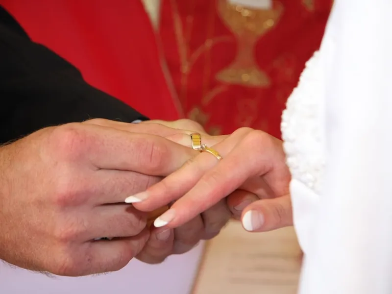 Zbliżenie: pan młody wsuwa złotą obrączkę na palec panny młodej