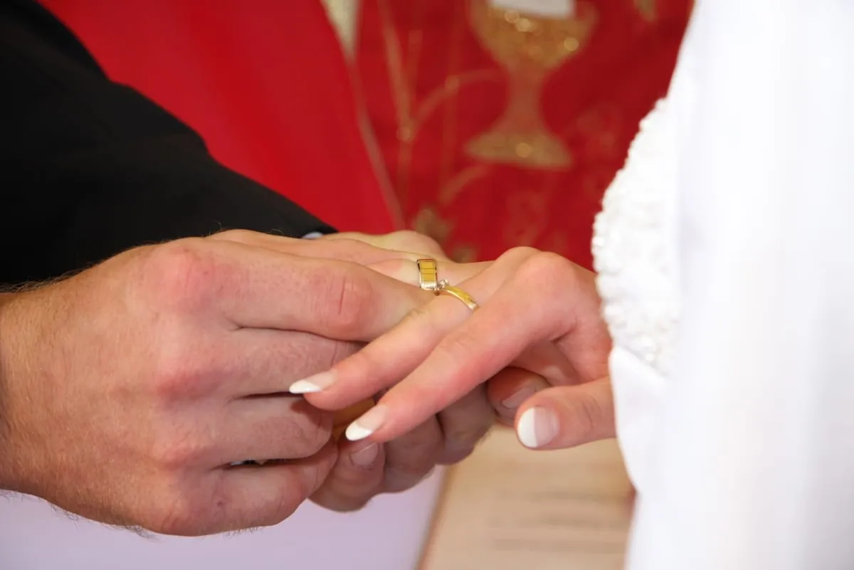 Zbliżenie: pan młody wsuwa złotą obrączkę na palec panny młodej