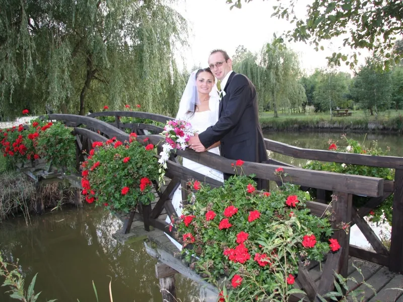 Para młoda w objęciach na mostku nad stawem, wokół kwitnące pelargonie